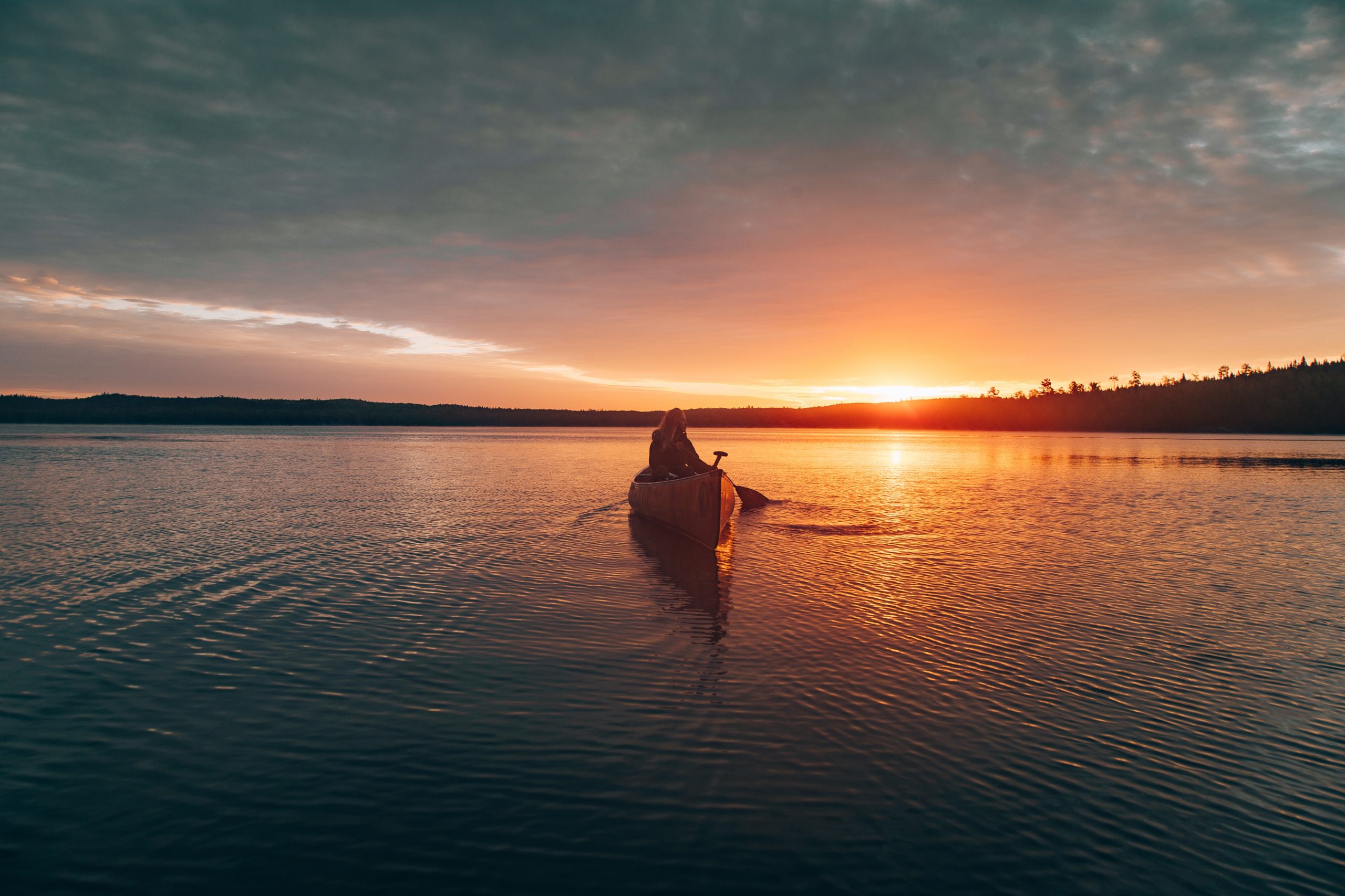 Beautiful distant shot of a female riding kayak in the middle of a lake during sunset